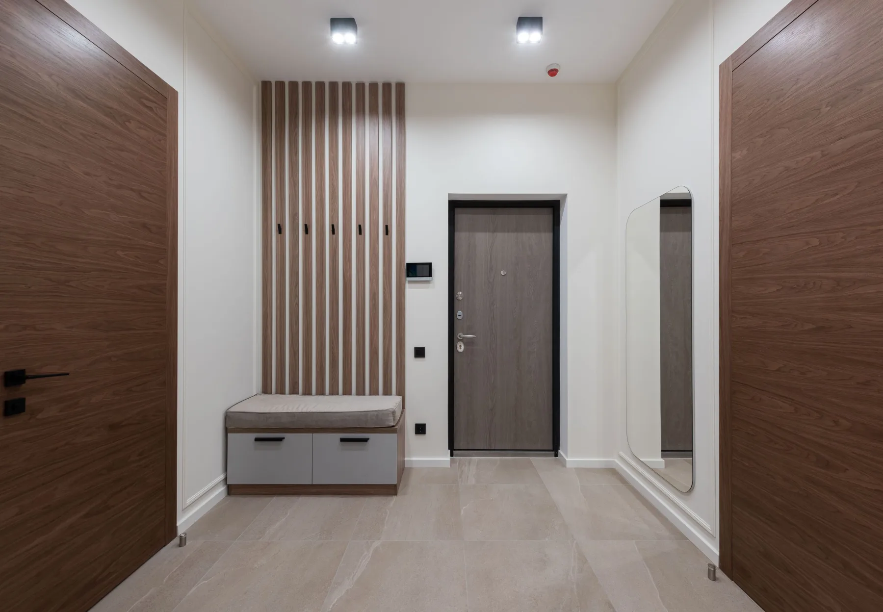 Interior view of a condo unit's entryway, showing the front door, a built-in coat rack, storage bench, and full-length mirror