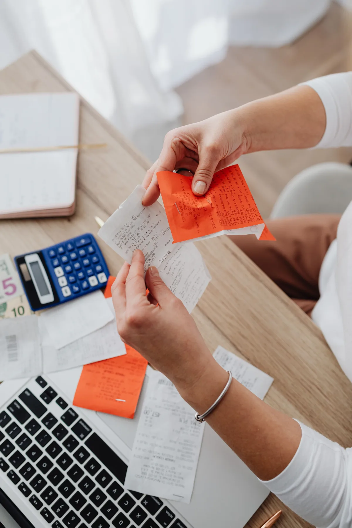 Close-up of hands sorting through a pile of paper receipts next to a calculator and laptop keyboard