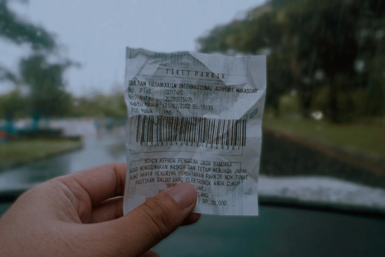 A hand holds up a crumpled, barcoded paper receipt outdoors, the kind of printed proof-of-payment slip issued at a payment counter.