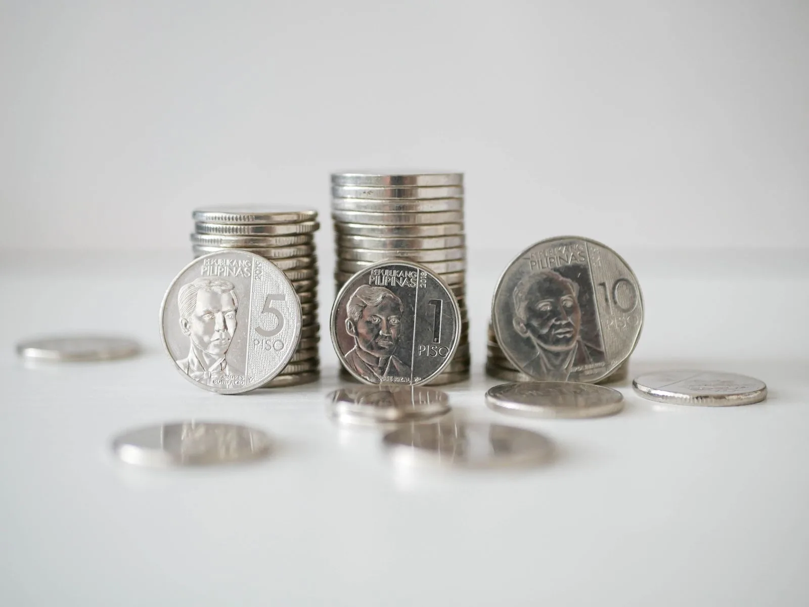 Stacks of Philippine one-peso, five-peso, and ten-peso coins standing upright on a plain white surface.