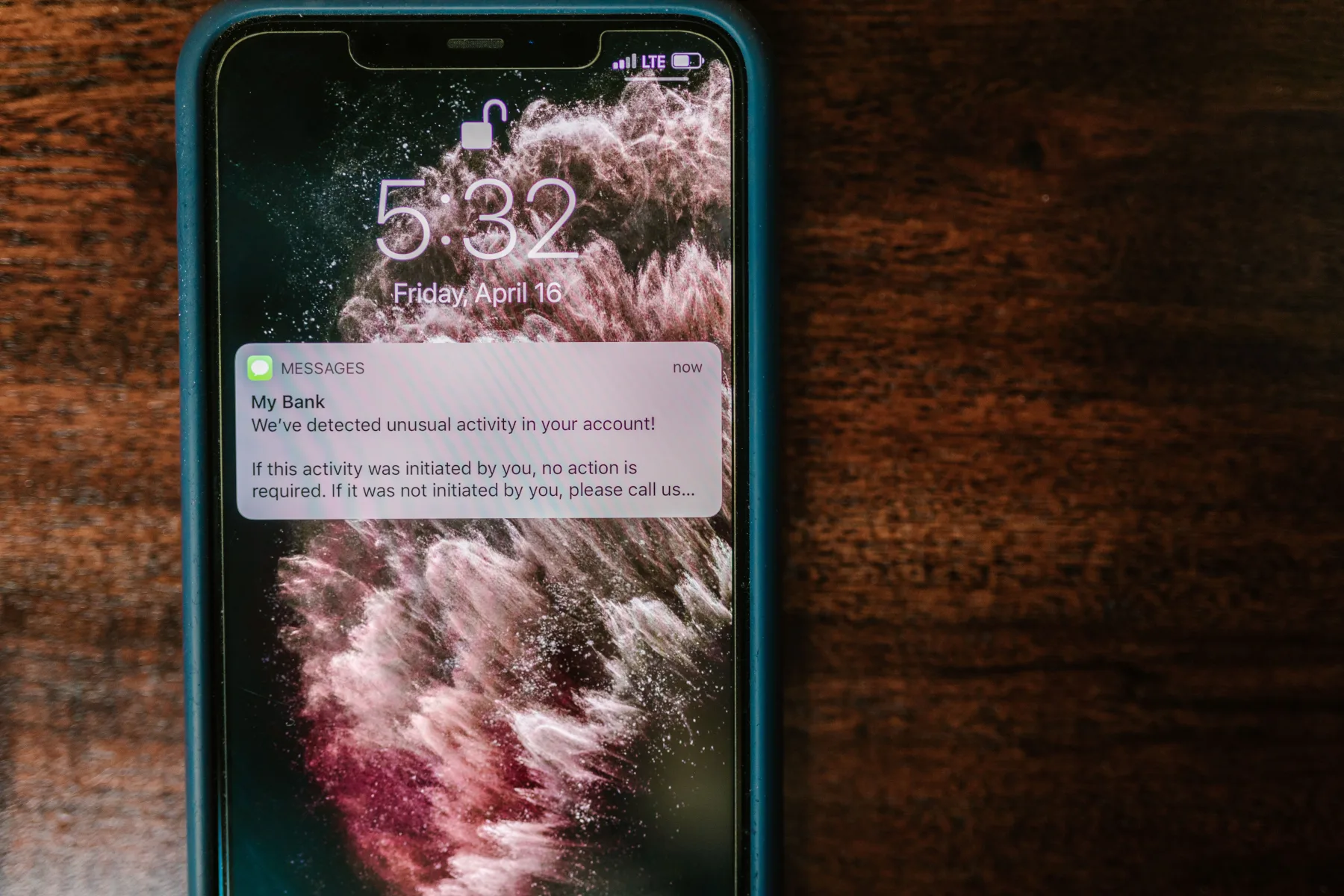 A smartphone lock screen at 5:32 on a Friday afternoon showing a message notification about unusual account activity, over a pink and dark abstract wallpaper