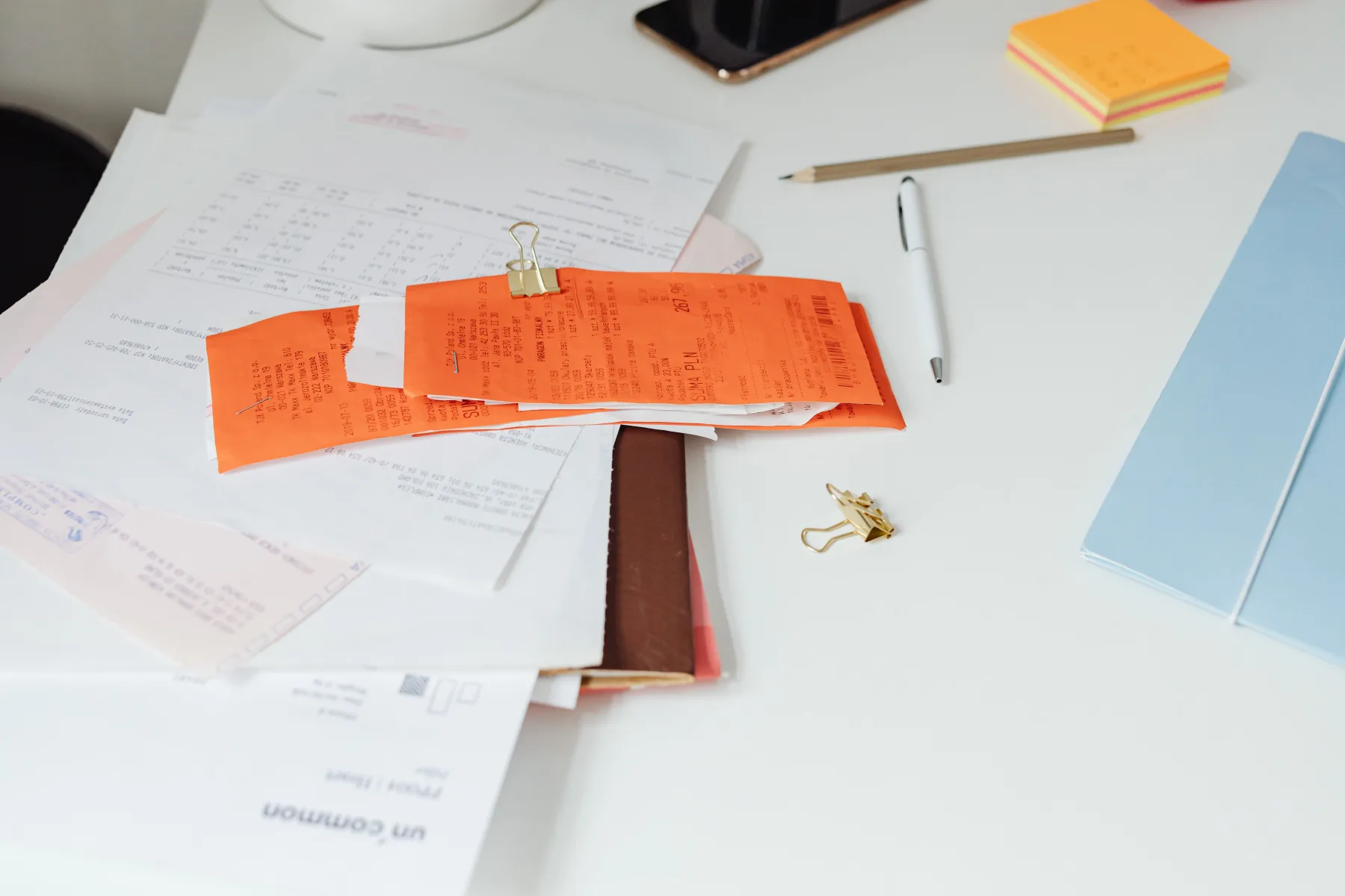 A cluttered desk covered with crumpled orange paper receipts, a notebook, and sticky notes