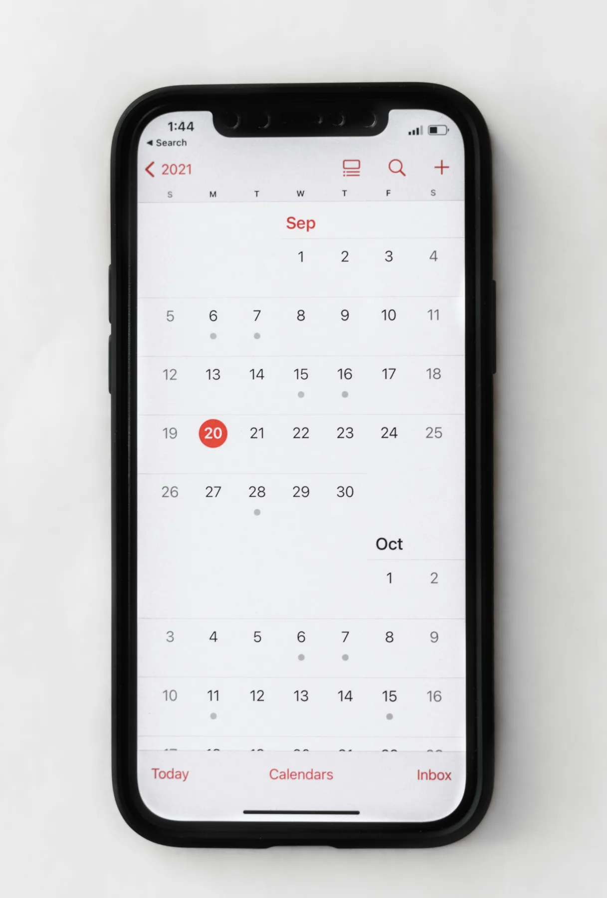 A smartphone lying on a white surface showing the Apple Calendar app open to September, with a few dates marked