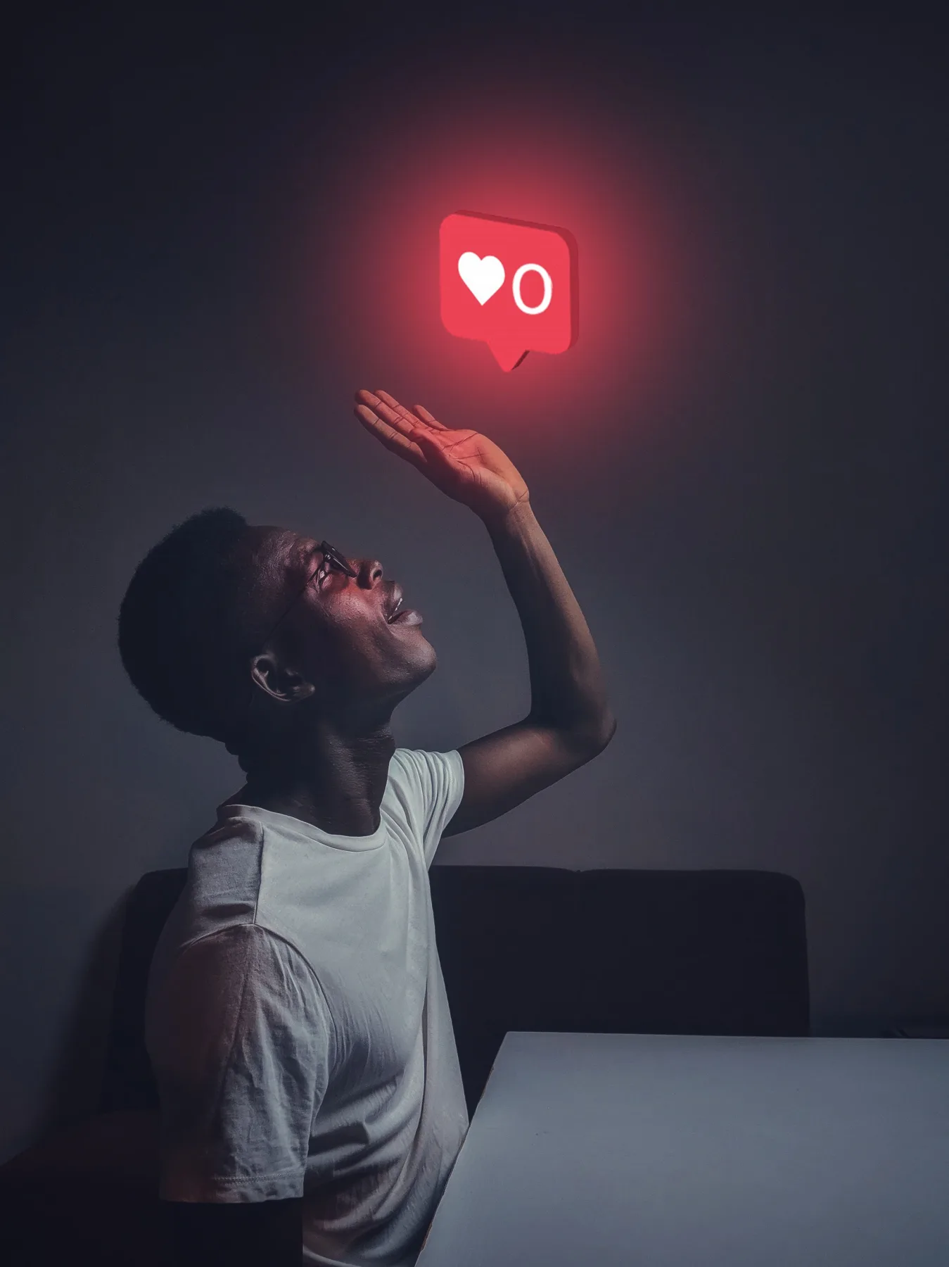 Man reaching up toward a glowing red heart notification icon floating above him in a dark room