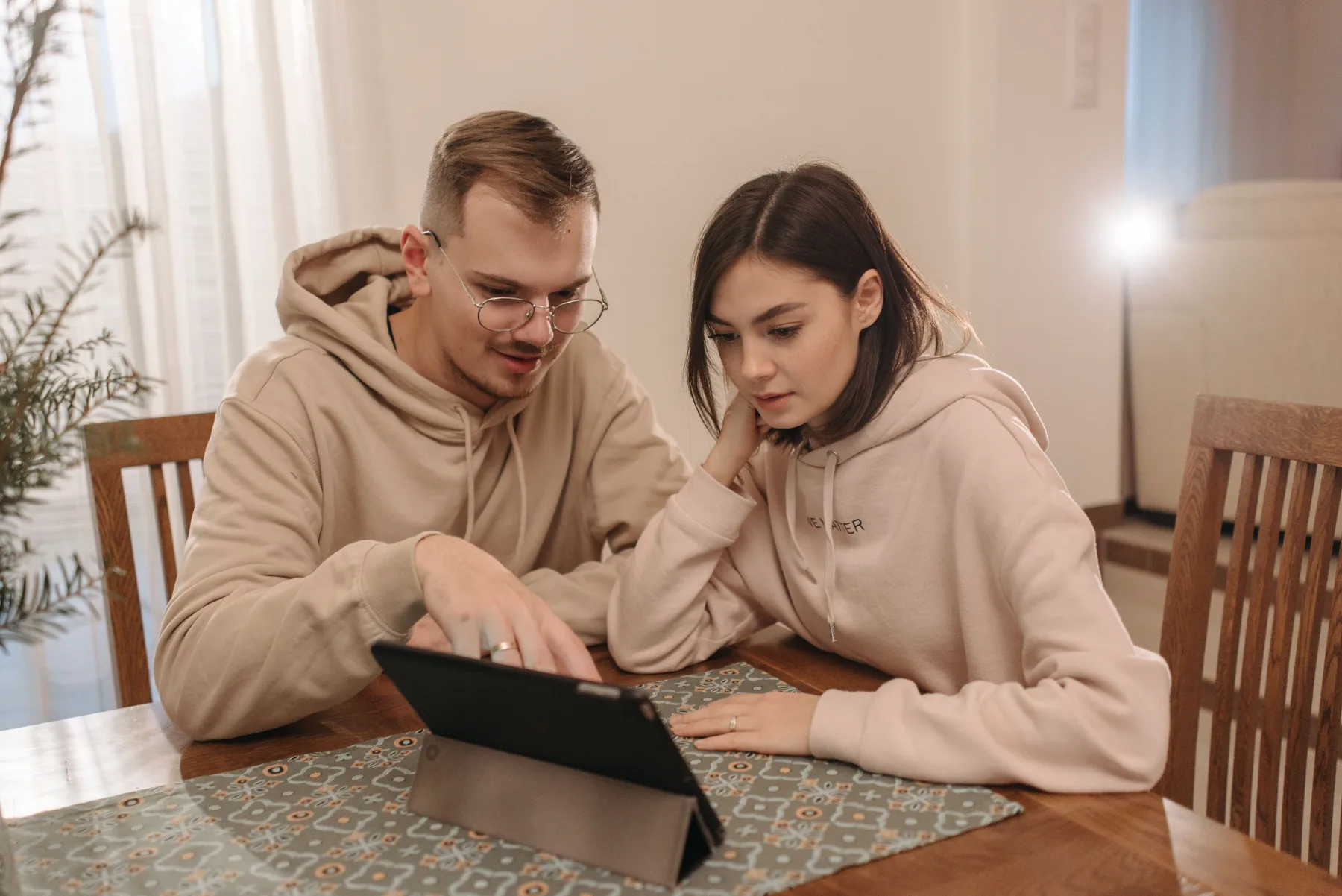A couple at a dining table looking closely at a tablet screen together