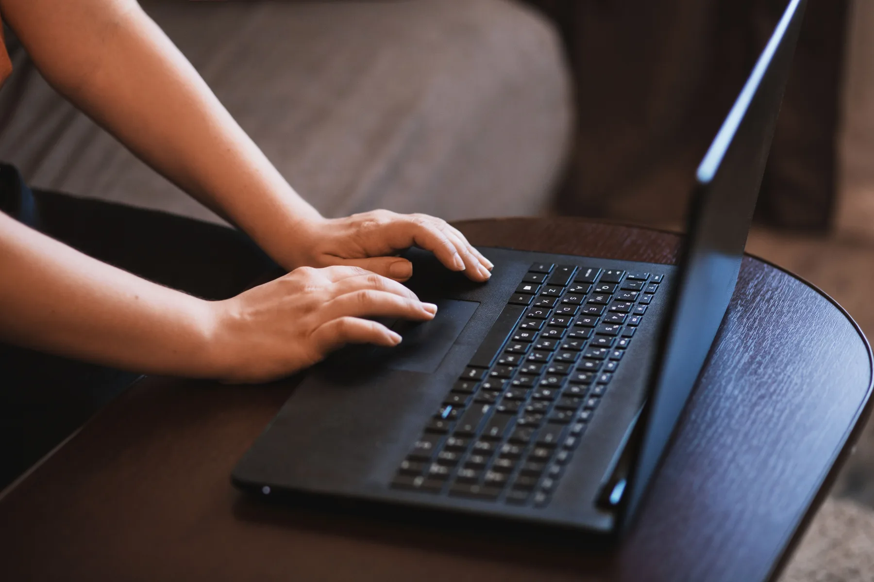 Close-up of two hands typing on a laptop keyboard resting on a small table