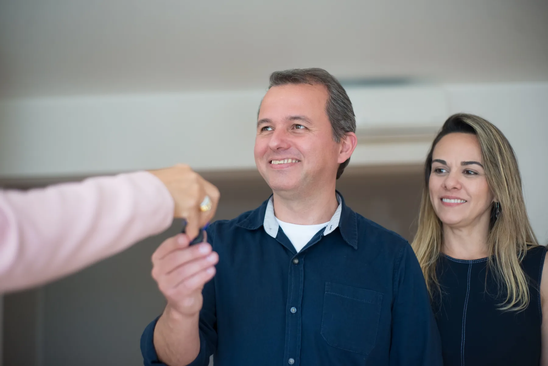 A person handing over a set of keys to a smiling couple standing in a kitchen