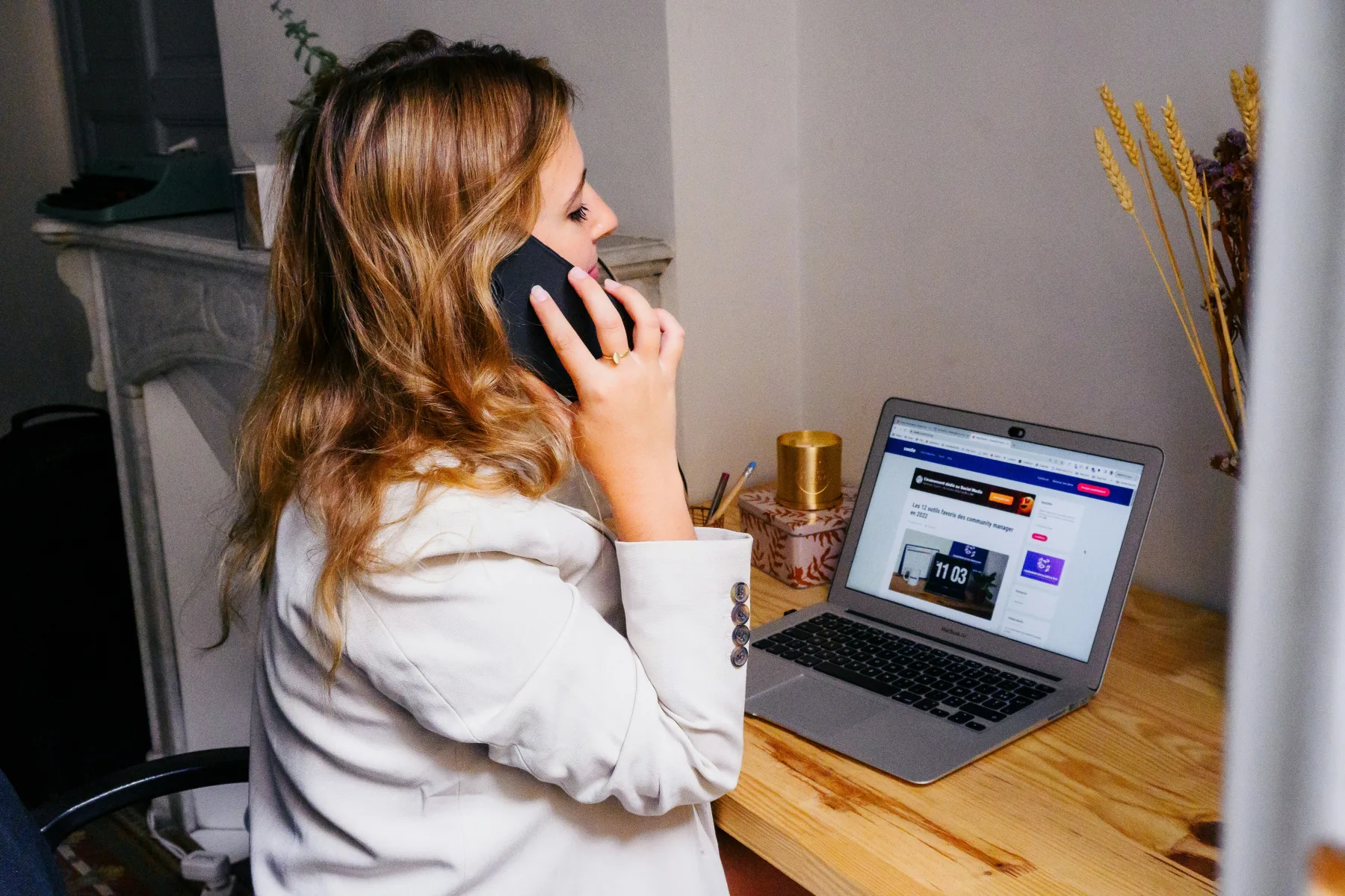 Woman on a phone call at a home desk with a laptop open in front of her