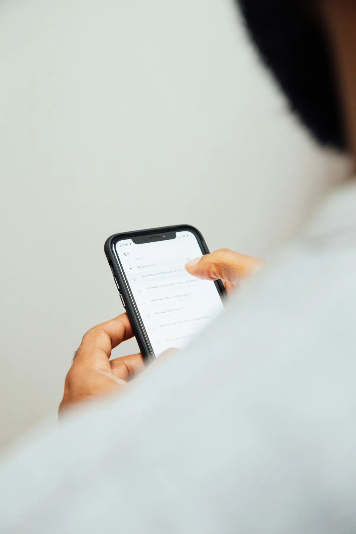 Person scrolling through a list of results on a smartphone, tapping an entry with their thumb