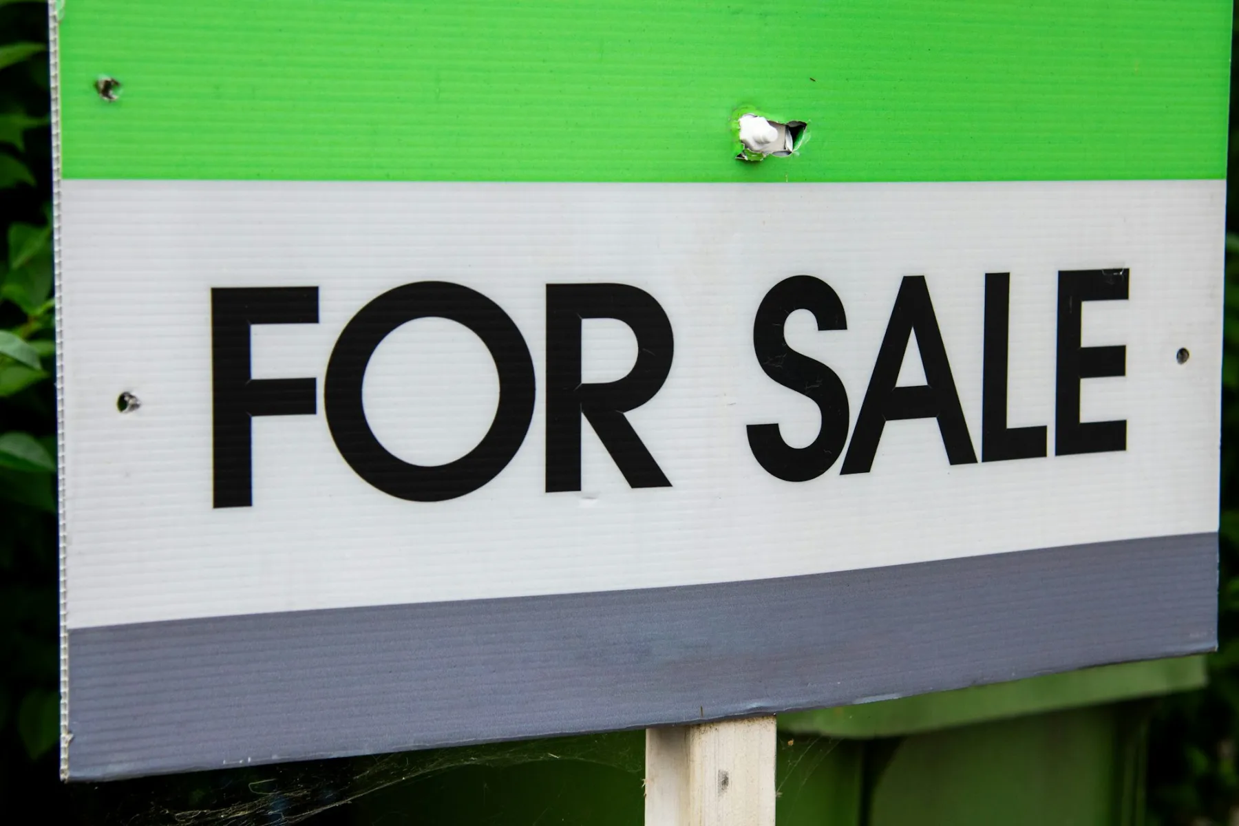Close-up of a green and white For Sale yard sign mounted on a wooden post