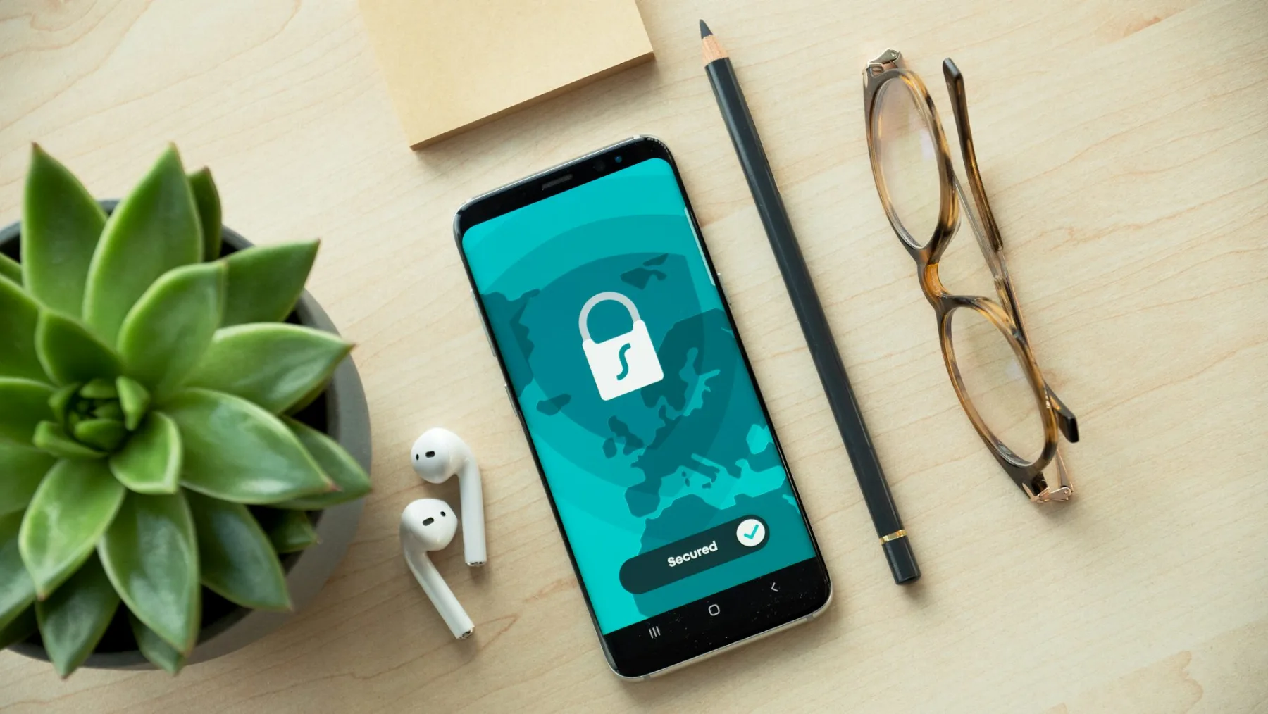Smartphone on a desk displaying a teal Secured screen with a padlock icon and checkmark