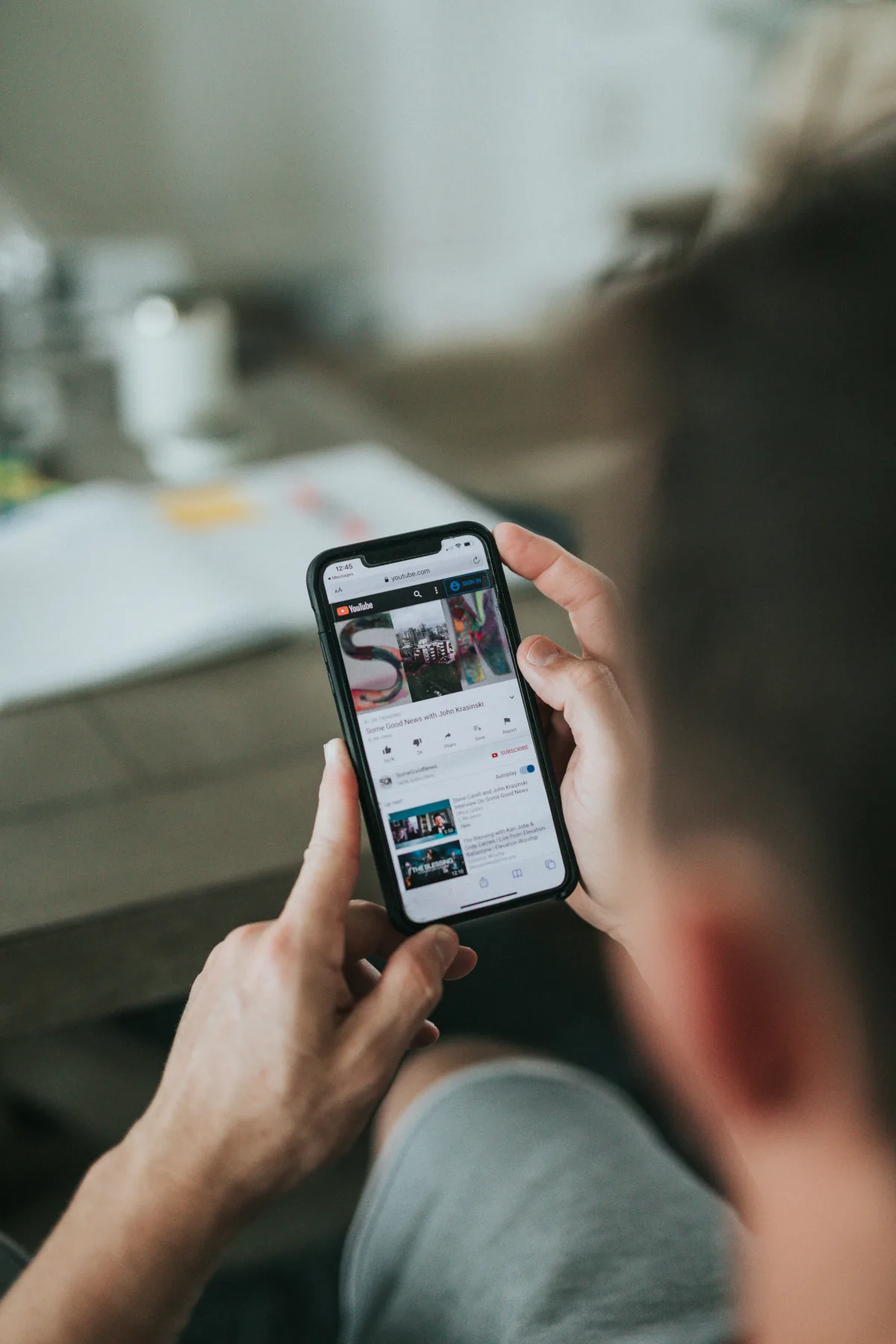 Over-the-shoulder view of a person holding an iPhone, watching a video on a webpage while sitting on a couch