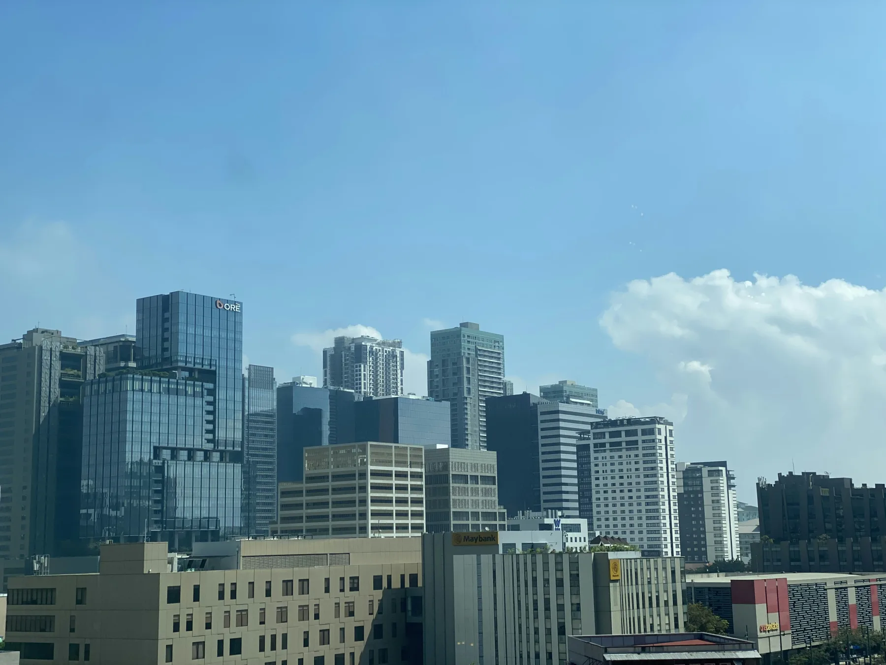 Skyline view of Metro Manila high-rise buildings under a clear blue sky, with the Maybank tower visible among the towers