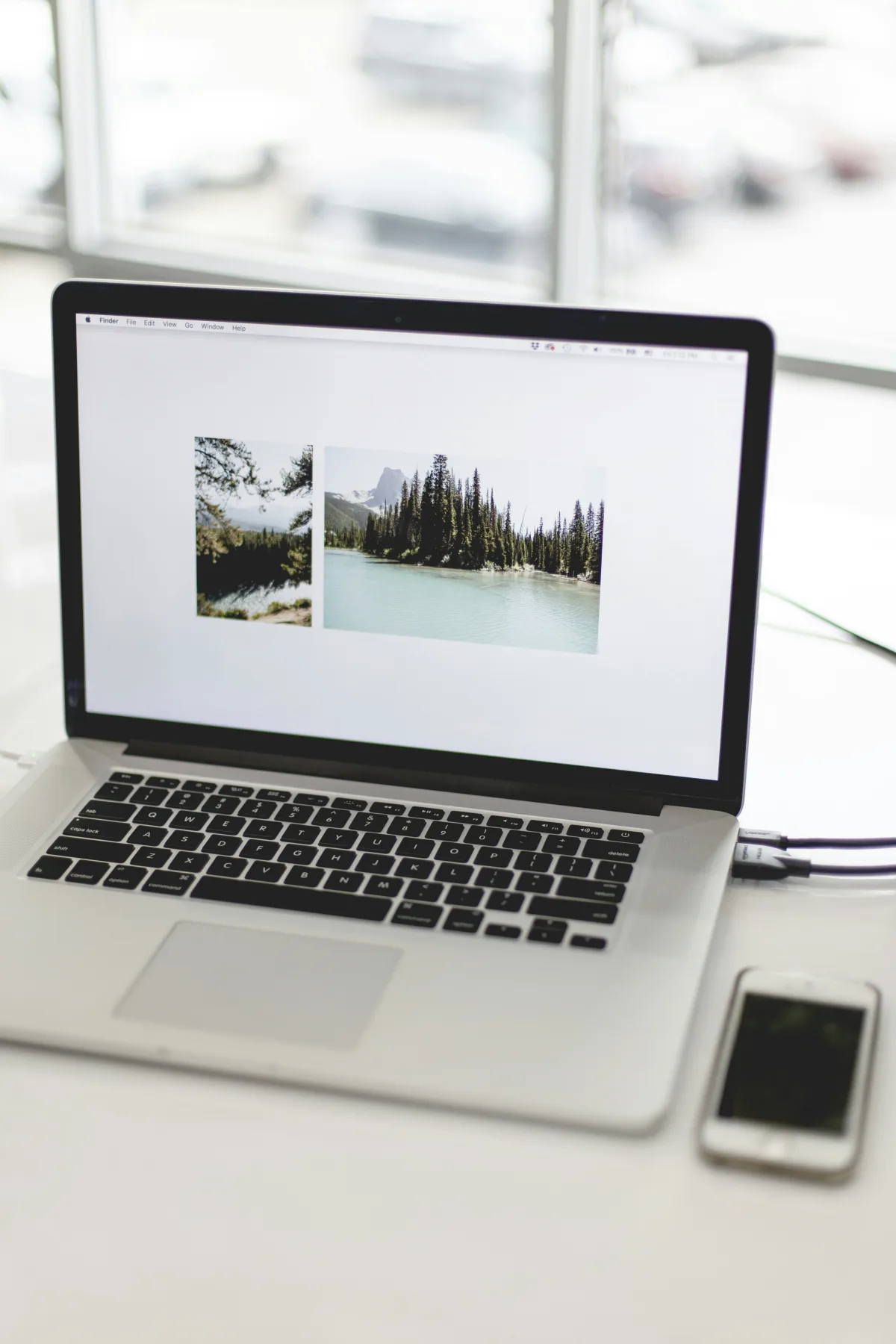 A laptop screen displaying two side-by-side nature photos open in Finder, with an iPhone resting on the desk beside the keyboard