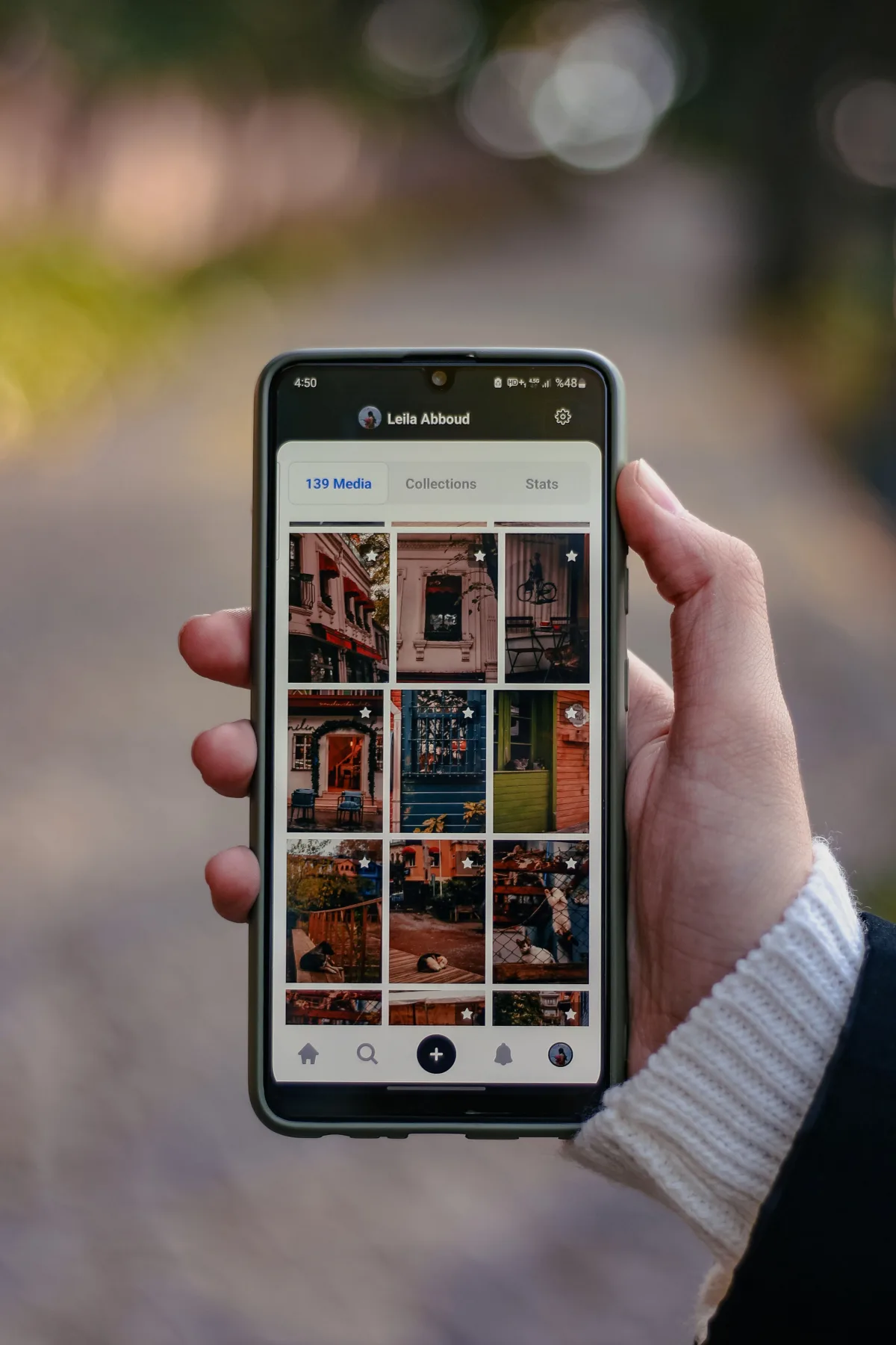 A hand holding a smartphone open to a photo grid on a social media profile, showing dozens of property and lifestyle photos in rows